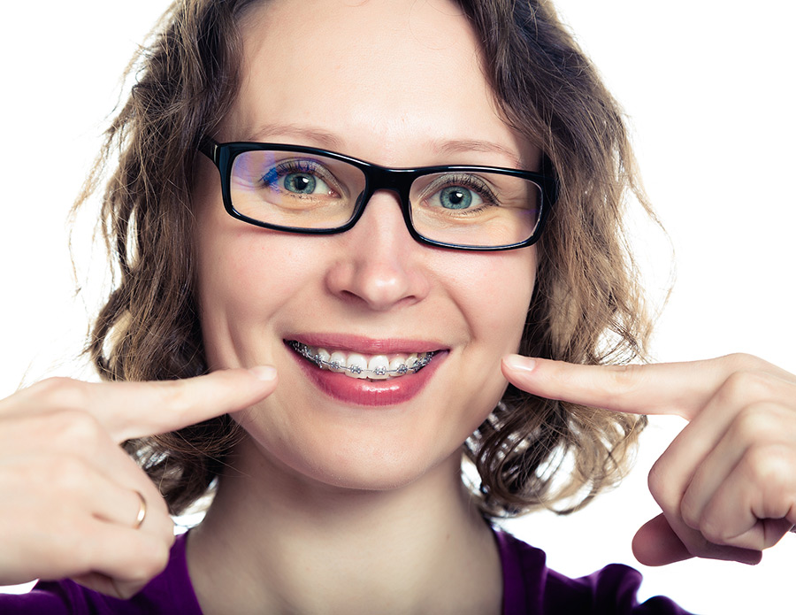 An adult woman pointing to her metal braces and smiling becasue her orthodontist offers payment plans